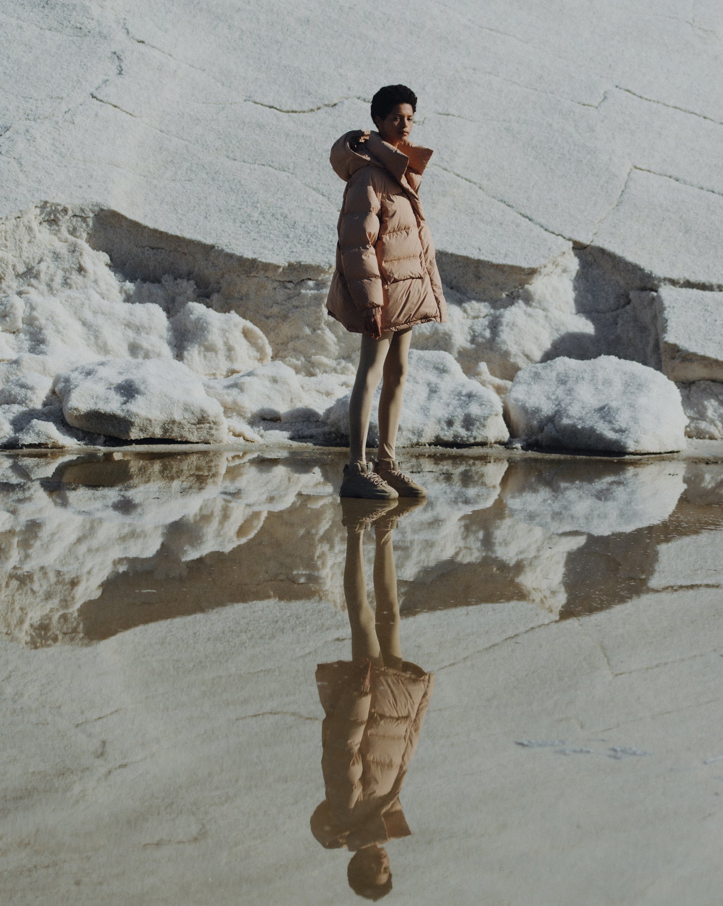 Model sanding on the snow capped mountain wearing the Val puffer jacket. Photographed by Charlotte Lapalus