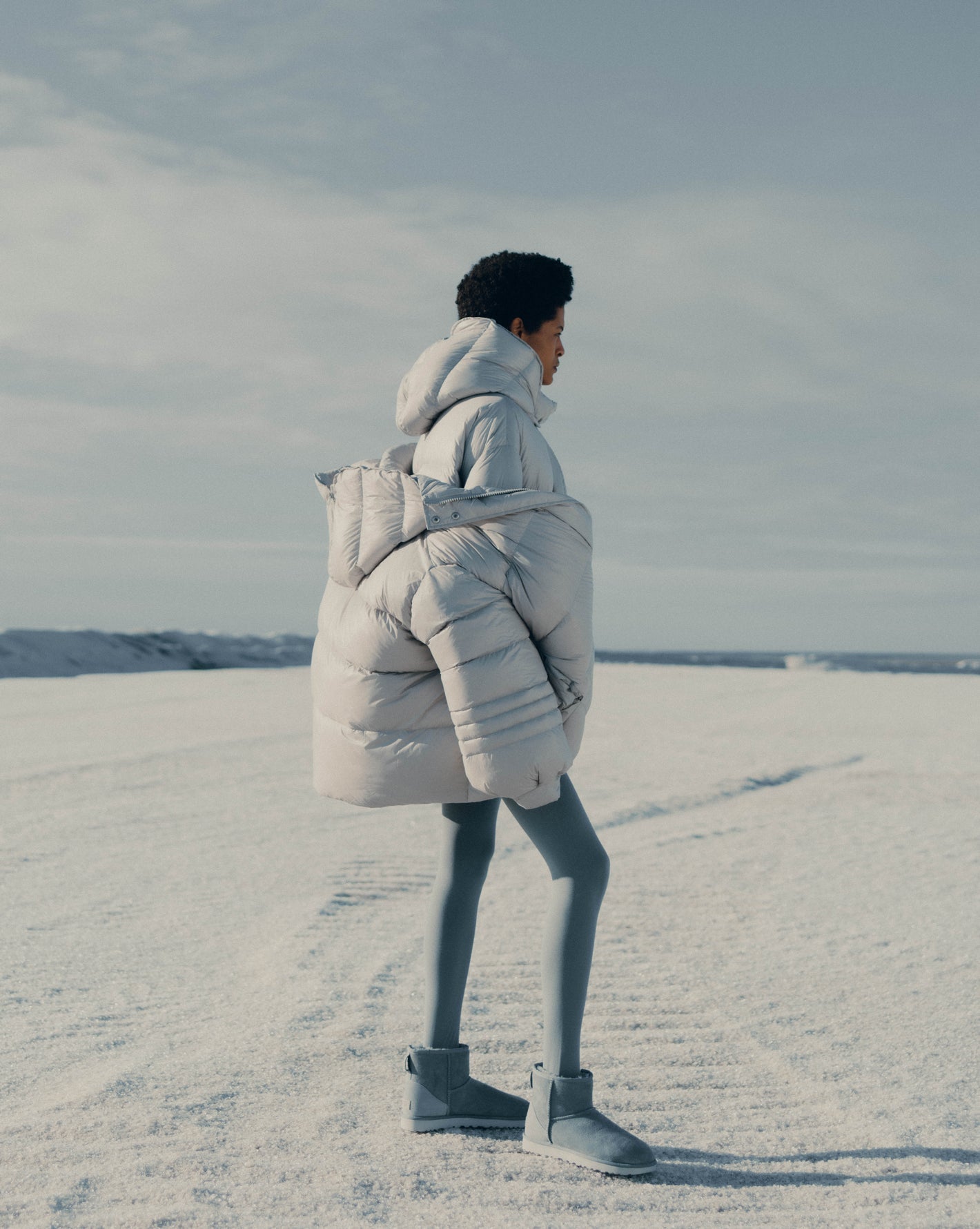 Model sanding on the snow capped mountain wearing two Val puffer jackets layered on top of each other. Photographed by Charlotte Lapalus