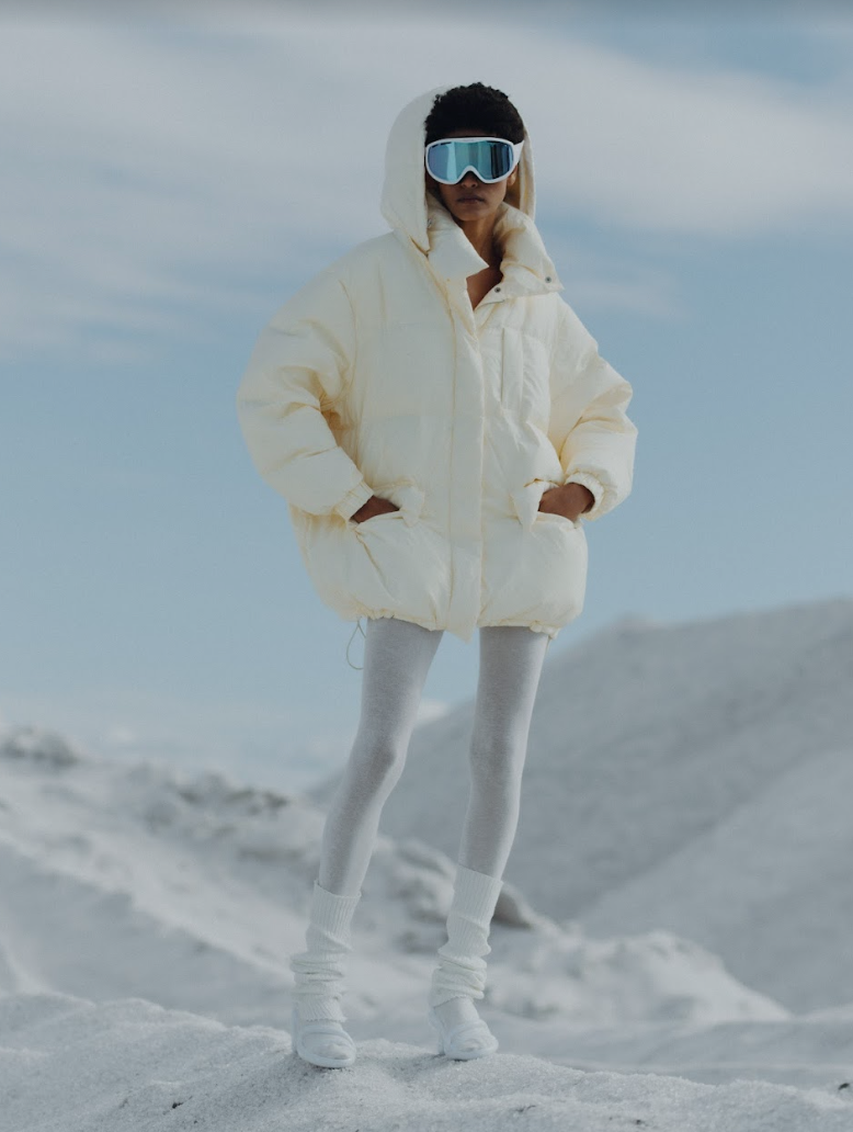 Model sanding on the snow capped mountain wearing the Val puffer jacket. Photographed by Charlotte Lapalus